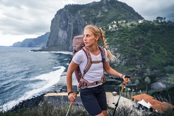Wanderin mit burgunderfarbenem Wanderrucksack vor einer dramatischen Küstenlandschaft.